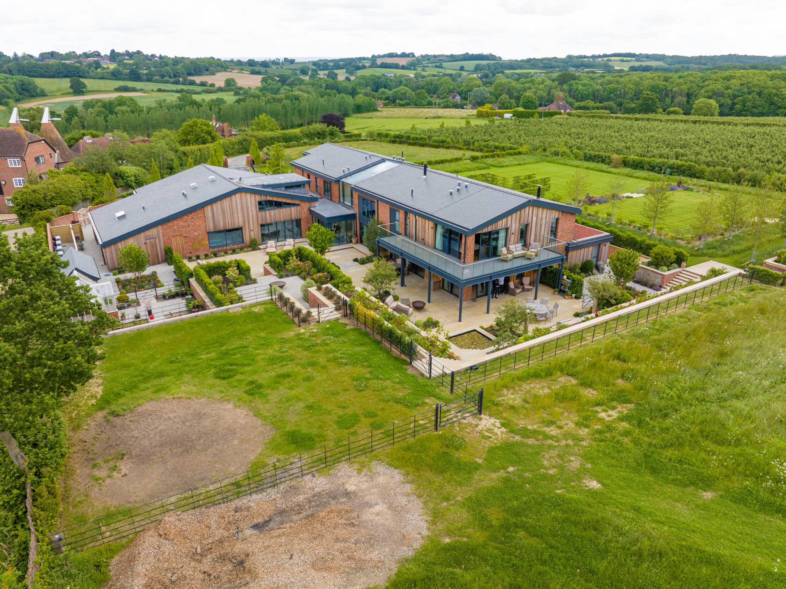 Aerial view of a modern, large house with multiple sections, featuring bespoke glass solutions like sliding doors and glass roofing, surrounded by landscaped gardens and green fields in a rural setting.
